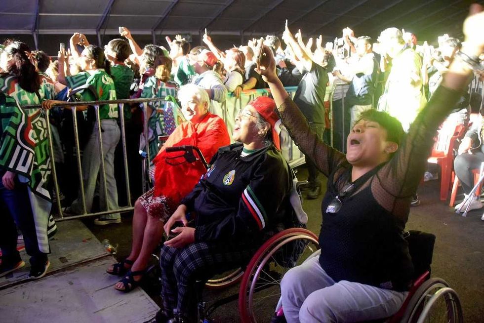 Dos mujeres en silla de ruedas levantan los brazos mientras disfrutan de un concierto en M\u00e9xicQ Fest.