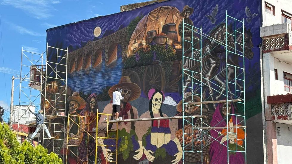Dos personas pintan un mural con calaveras y motivos de D\u00eda de Muertos en San Juan del R\u00edo