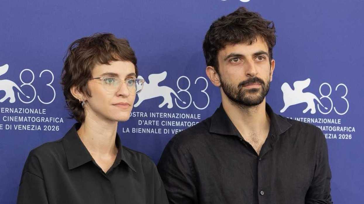 Dos personas posan de negro ante el fondo de la Mostra Internacional de Arte Cinematográfico de Venecia 2026