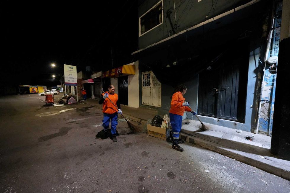 Dos trabajadoras de Servicios P\u00fablicos barren una calle de Quer\u00e9taro durante la madrugada con cartel de Plan de Obra al fondo