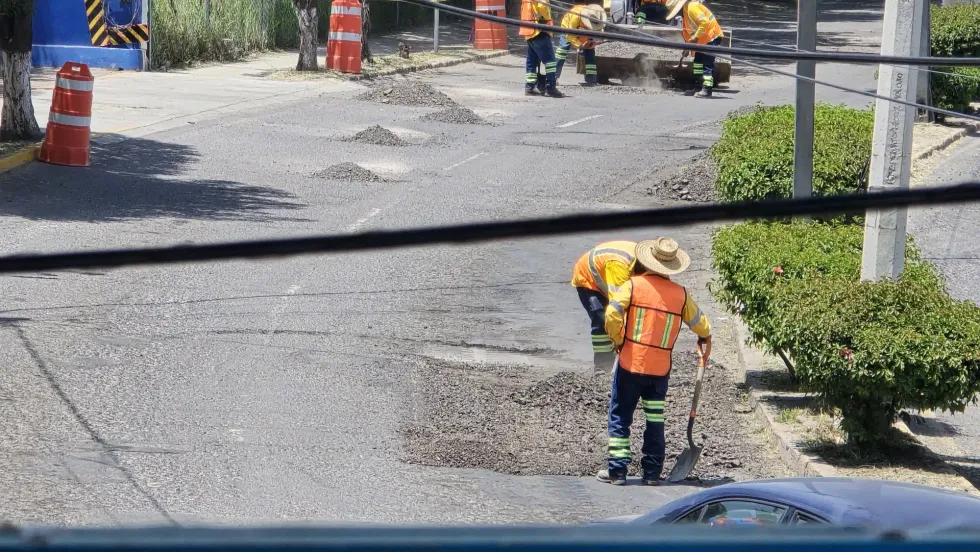 Dos trabajadores con chalecos reflectantes junto a miniexcavadora Bobcat durante trabajos de reparaci\u00f3n vial en San Juan del R\u00edo.