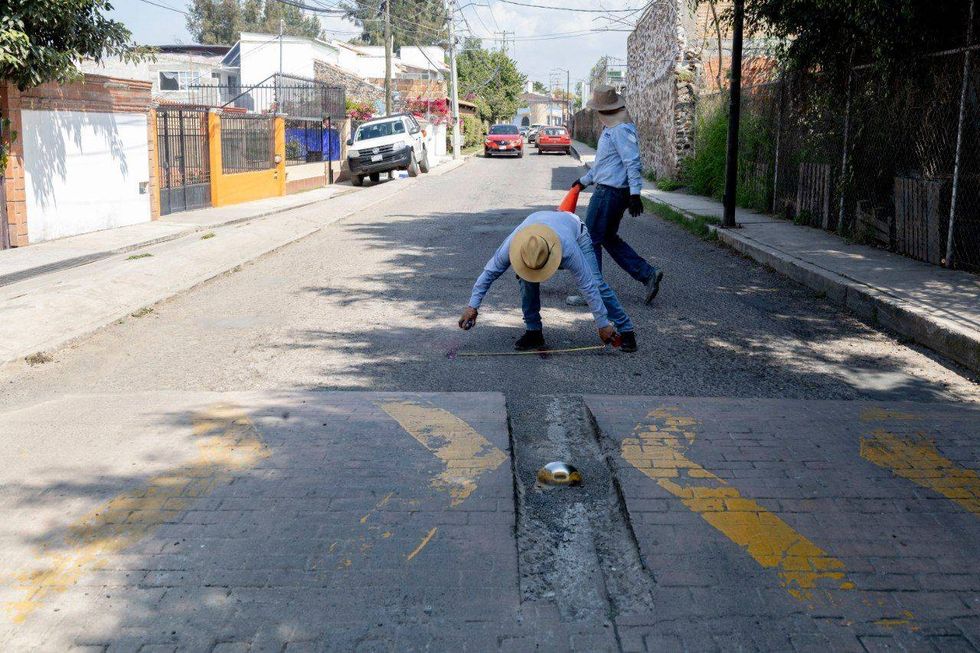 Dos trabajadores marcan el asfalto con cinta m\u00e9trica y pintura en aerosol junto a un cono y un tope.