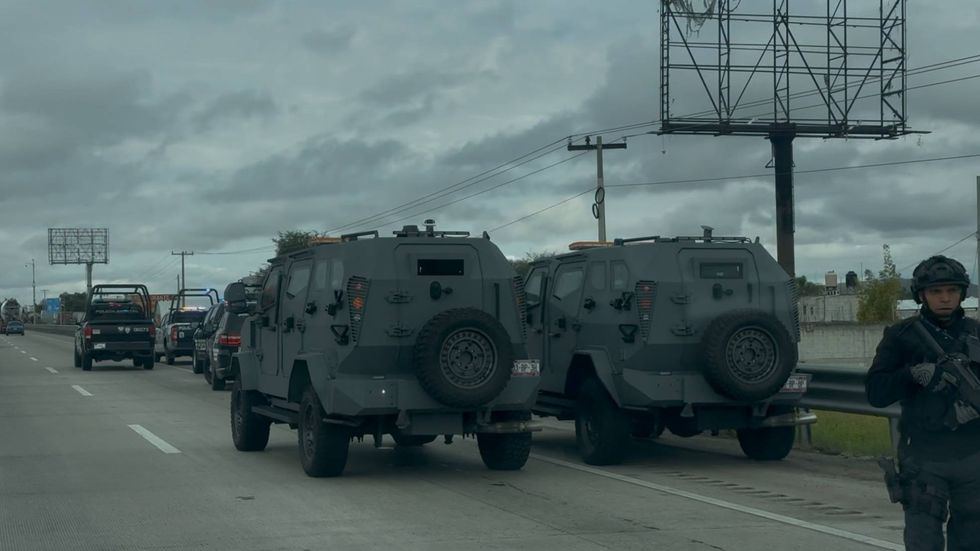 Dos veh\u00edculos blindados grises con neum\u00e1tico de refacci\u00f3n en la parte trasera permanecen detenidos en la autopista M\u00e9xico-Quer\u00e9taro, custodiados por un polic\u00eda con arma larga.