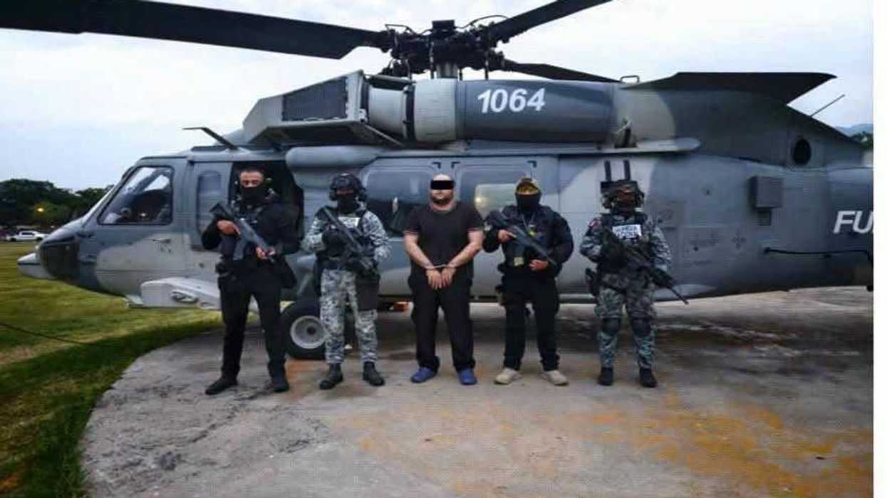 Edgar Valeriano N, alias Kamoni, esposado entre agentes federales frente a un helicóptero tras su detención en Tepalcatepec