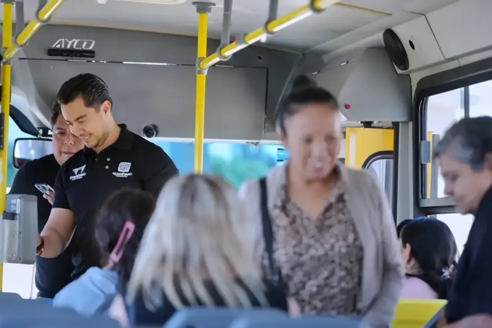 El alcalde Felifer Mac\u00edas revisa un dispositivo junto a una funcionaria en el interior de un autob\u00fas del Transporte Comunitario Gratuito de Quer\u00e9taro, mientras usuarios viajan sentados al fondo