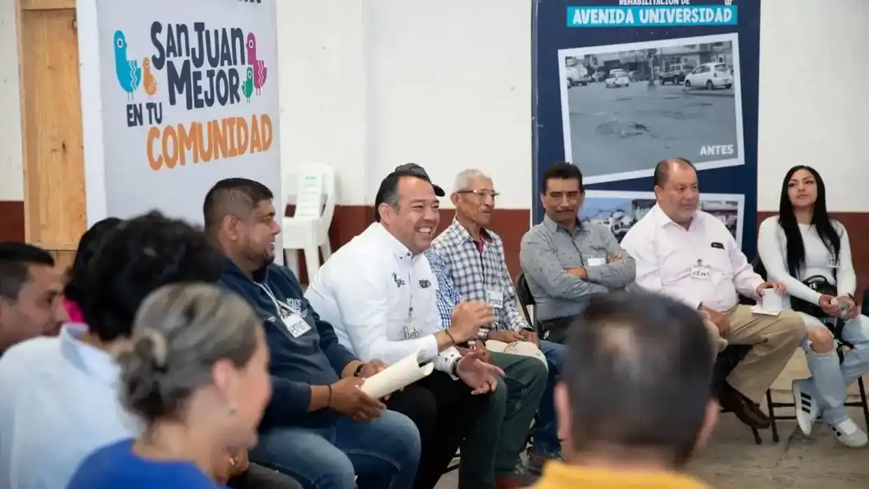 El alcalde Roberto Cabrera Valencia en reunión con liderazgos de la comunidad de Paso de Mata, con banners del programa San Juan Mejor en tu Comunidad y rehabilitación de Avenida Universidad al fondo