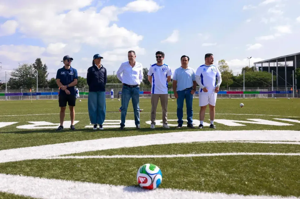 El gobernador Mauricio Kuri Gonz\u00e1lez, al centro, posa junto a Oribe Peralta y otros funcionarios del INDEREQ en la cancha de pasto sint\u00e9tico de la unidad deportiva, con un bal\u00f3n de f\u00fatbol en primer plano.