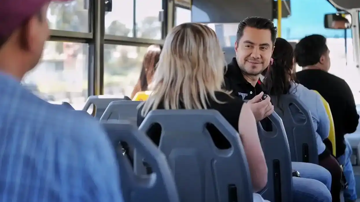El presidente municipal Felifer Macías conversa con beneficiarias del Transporte Comunitario Gratuito en una parada de la delegación Santa Rosa Jáuregui, con un autobús del sistema al fondo