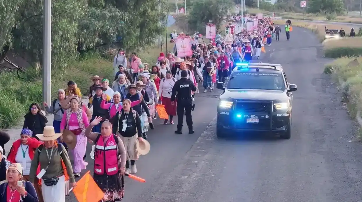 Elemento de la POES y personal de Protección Civil estatal observan el avance del contingente femenino frente al escenario de la concentración, con la leyenda "Viva Cristo, Rey del Universo" visible al fondo