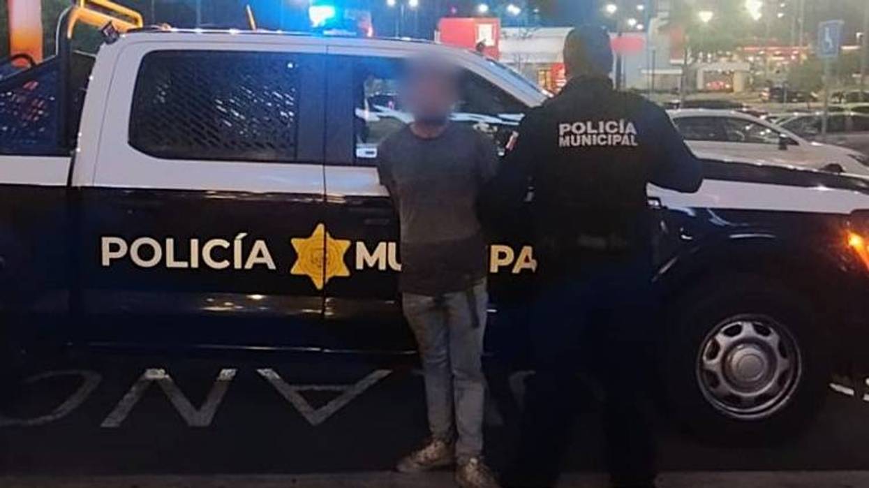 Elemento de la Policía Municipal de Querétaro y un hombre detenido, con el rostro difuminado, junto a una patrulla.