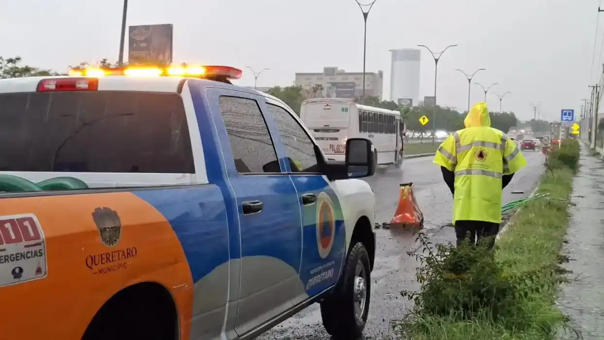 Elemento de Protección Civil municipal de Querétaro y unidad 911 de emergencias en una avenida bajo la lluvia