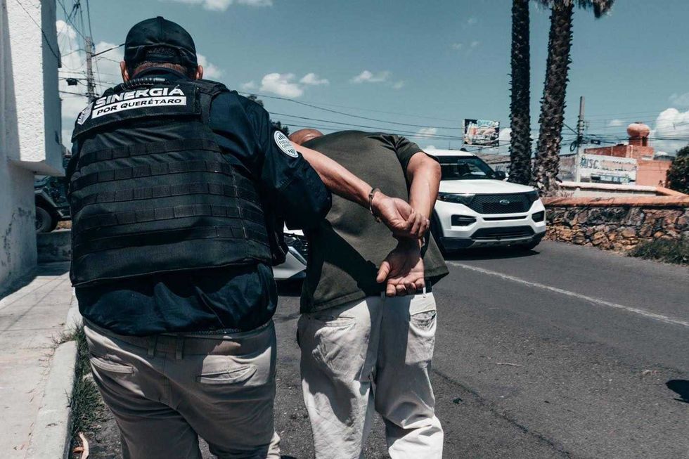 Elemento de seguridad custodia a una persona detenida durante cateos de Sinergia por Quer\u00e9taro.