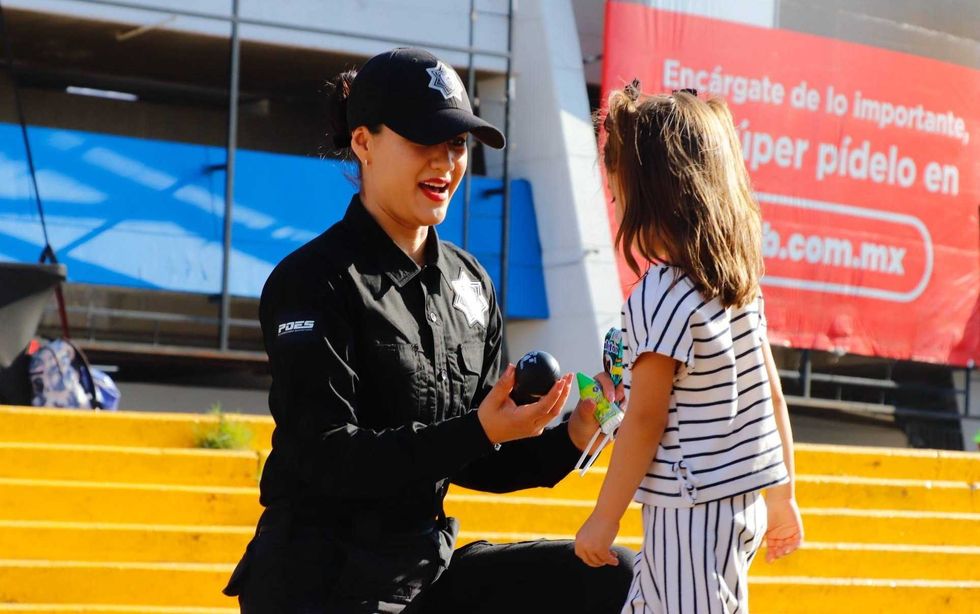 Elemento femenina de la Polic\u00eda Estatal de Quer\u00e9taro interact\u00faa con una ni\u00f1a en un espacio p\u00fablico.