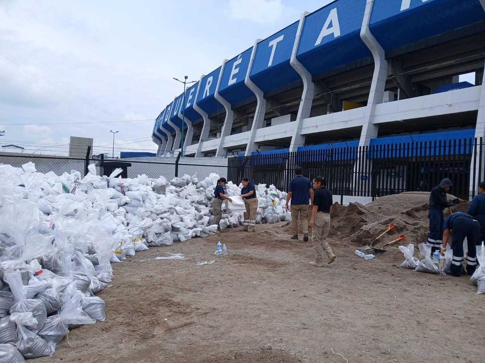 Elementos de Bomberos y Protecci\u00f3n Civil llenan costales de arena junto a un mont\u00edculo frente al Estadio Corregidora