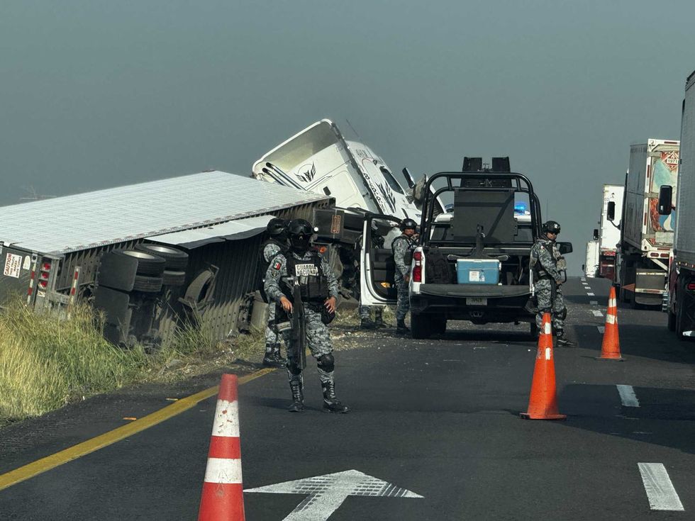 Elementos de la Guardia Nacional vigilan el sitio donde un tractocami\u00f3n y su caja seca quedaron volcados sobre el divisor central de la carretera.