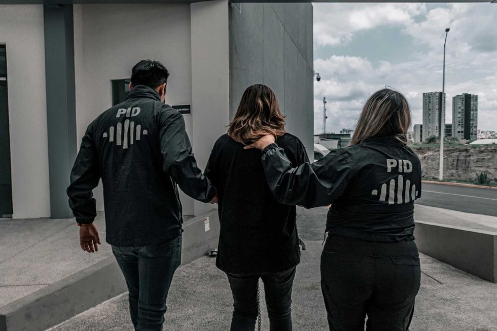 Elementos de la Polic\u00eda de Investigaci\u00f3n del Delito trasladan caminando a una persona detenida hacia un veh\u00edculo oficial.