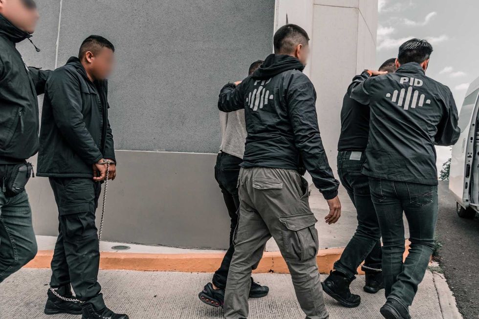 Elementos de la Polic\u00eda de Investigaci\u00f3n del Delito trasladan caminando a una persona detenida hacia un veh\u00edculo oficial.
