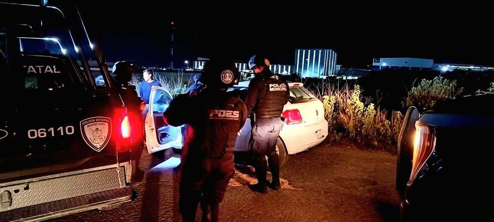 Elementos de la Polic\u00eda Estatal de Quer\u00e9taro y la Polic\u00eda Municipal revisan un veh\u00edculo particular durante la noche, con las puertas abiertas y una persona de pie junto a la unidad.