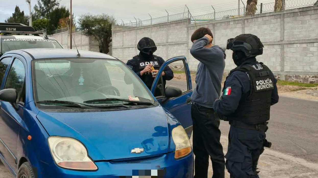 Elementos de la Policía Municipal y del grupo G.O.E.S. realizan una revisión a un hombre junto a un automóvil azul durante el operativo de seguridad en San Juan del Río.