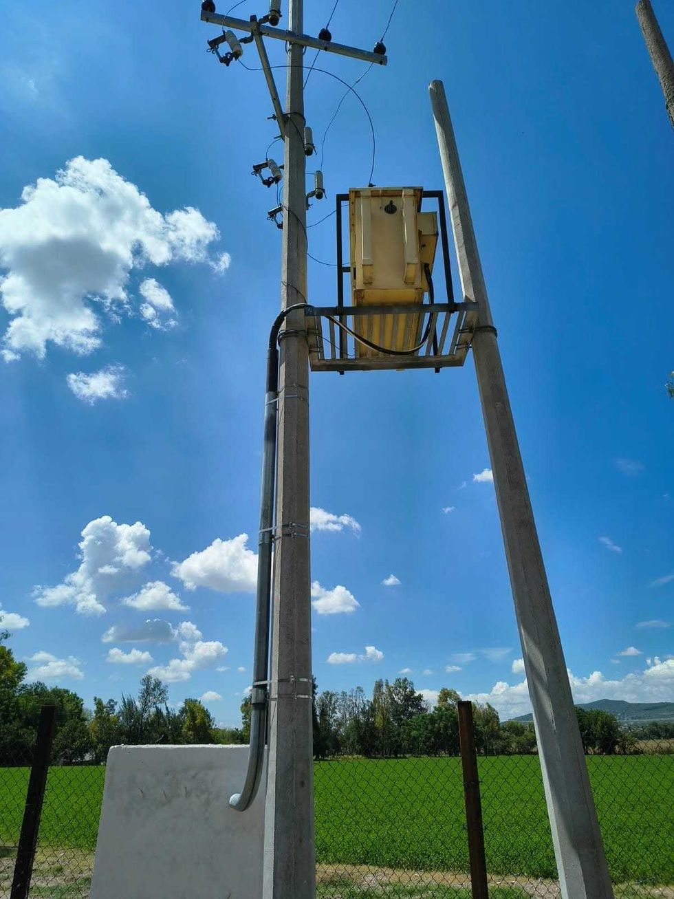 Equipo el\u00e9ctrico montado en un poste de concreto junto a una parcela verde en la unidad de riego Pozo del Alto de Guadalupe, San Juan del R\u00edo