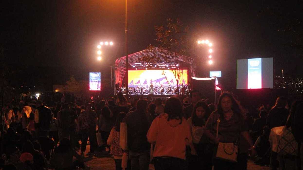 Escenario de Sinfonía en La Queretana de noche, con una orquesta, pantallas laterales y público en primer plano.