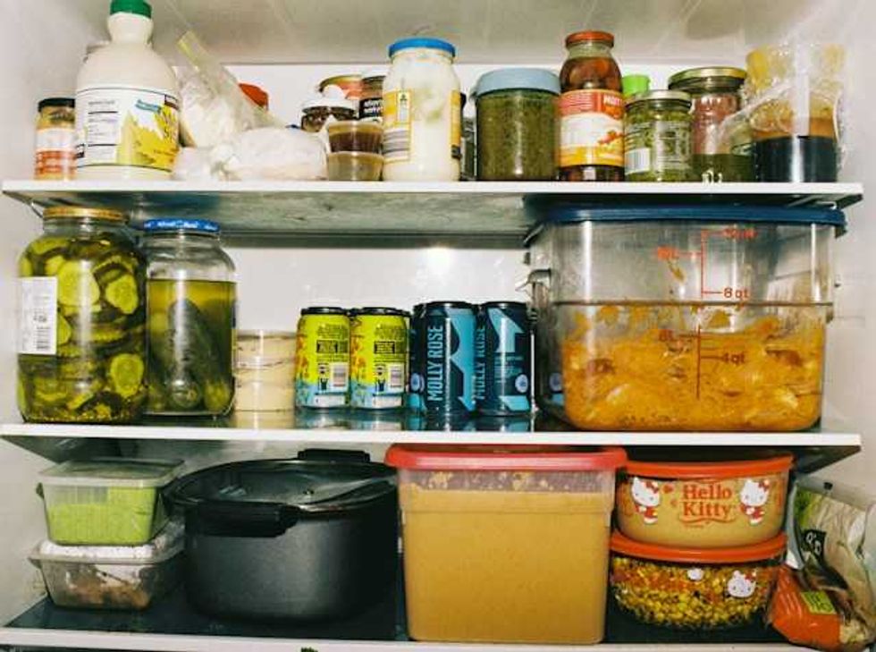 Estantes de refrigerador con frascos, recipientes con tapa, latas y una olla, acomodados en tres niveles