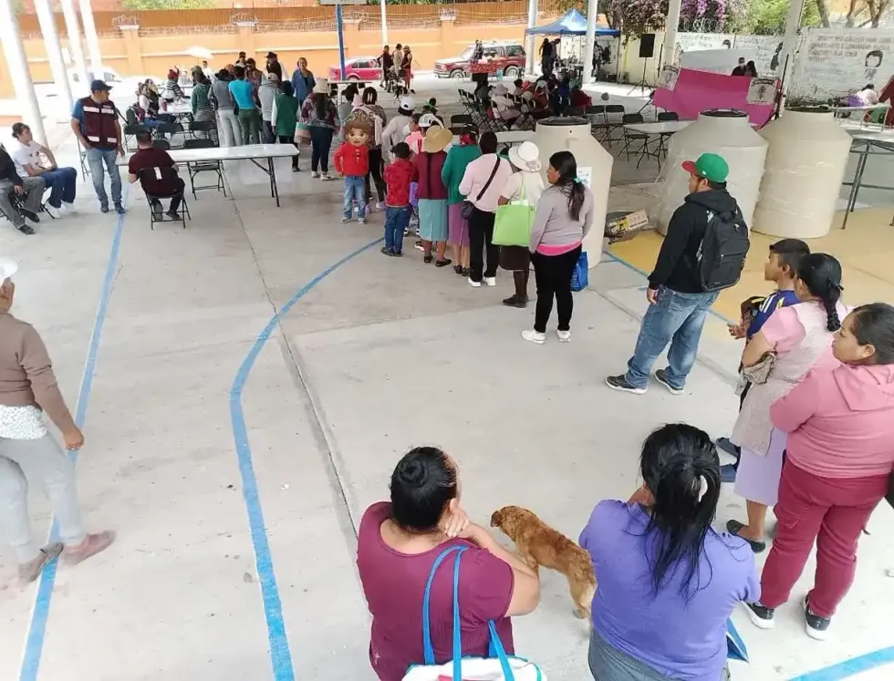 Familias forman fila junto a mesas de atenci\u00f3n y tinacos bajo un techado