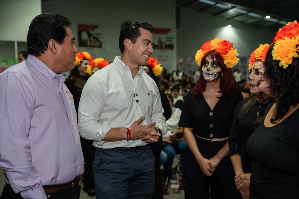 Felifer Mac\u00edas con dos hombres y catrinas y un charro catrino ante el fondo \u201cNuestra Cultura Nos Une\u201d del SNTE Secci\u00f3n 24.