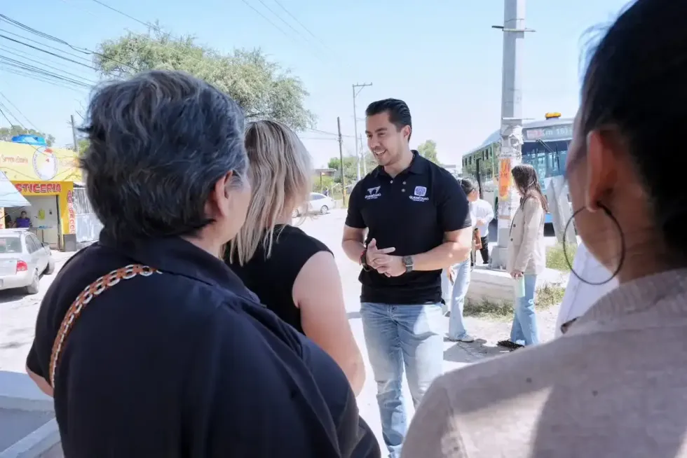 Felifer Mac\u00edas con playera negra institucional conversa con pasajeros sentados en el interior de un autob\u00fas del Transporte Comunitario Gratuito de Quer\u00e9taro