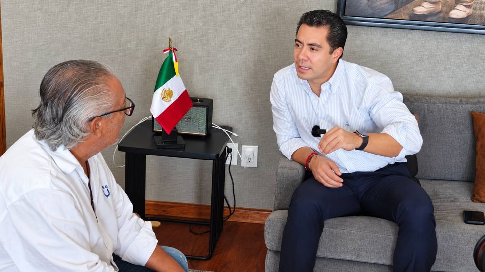 Felifer Mac\u00edas Olvera, presidente municipal de Quer\u00e9taro, conversa con un periodista durante una entrevista en su oficina, junto a una bandera de M\u00e9xico.