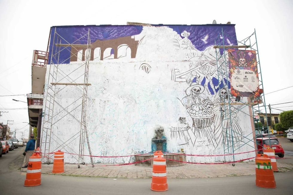 Figuras de esqueletos con una canasta en el Mural de D\u00eda de Muertos de San Juan del R\u00edo, junto a una lona de patrocinio