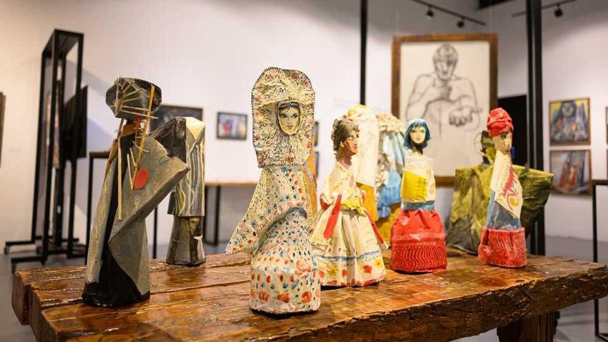 Figuras pintadas a mano con vestidos de colores sobre una mesa de madera en la retrospectiva de Daniel Manrique en Tepito