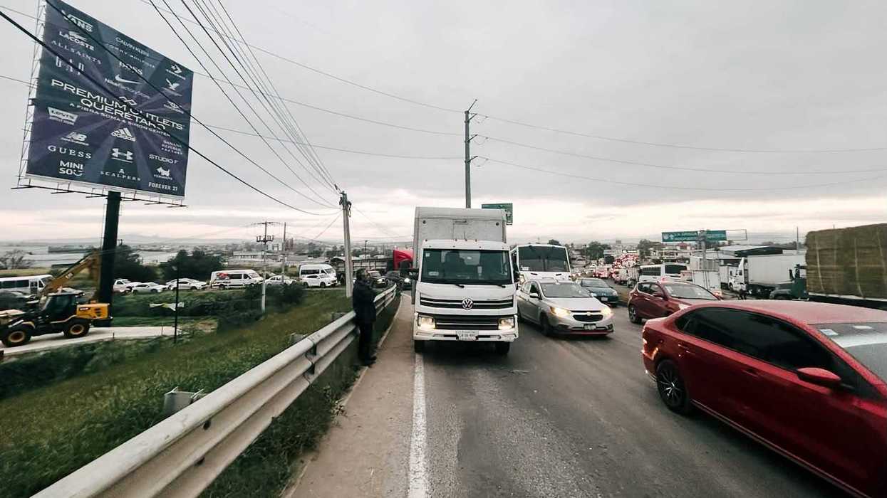 Fila de automóviles, camiones y transporte de personal en la vialidad de acceso al puente de La Piedad, en El Marqués, Querétaro, bajo cielo nublado