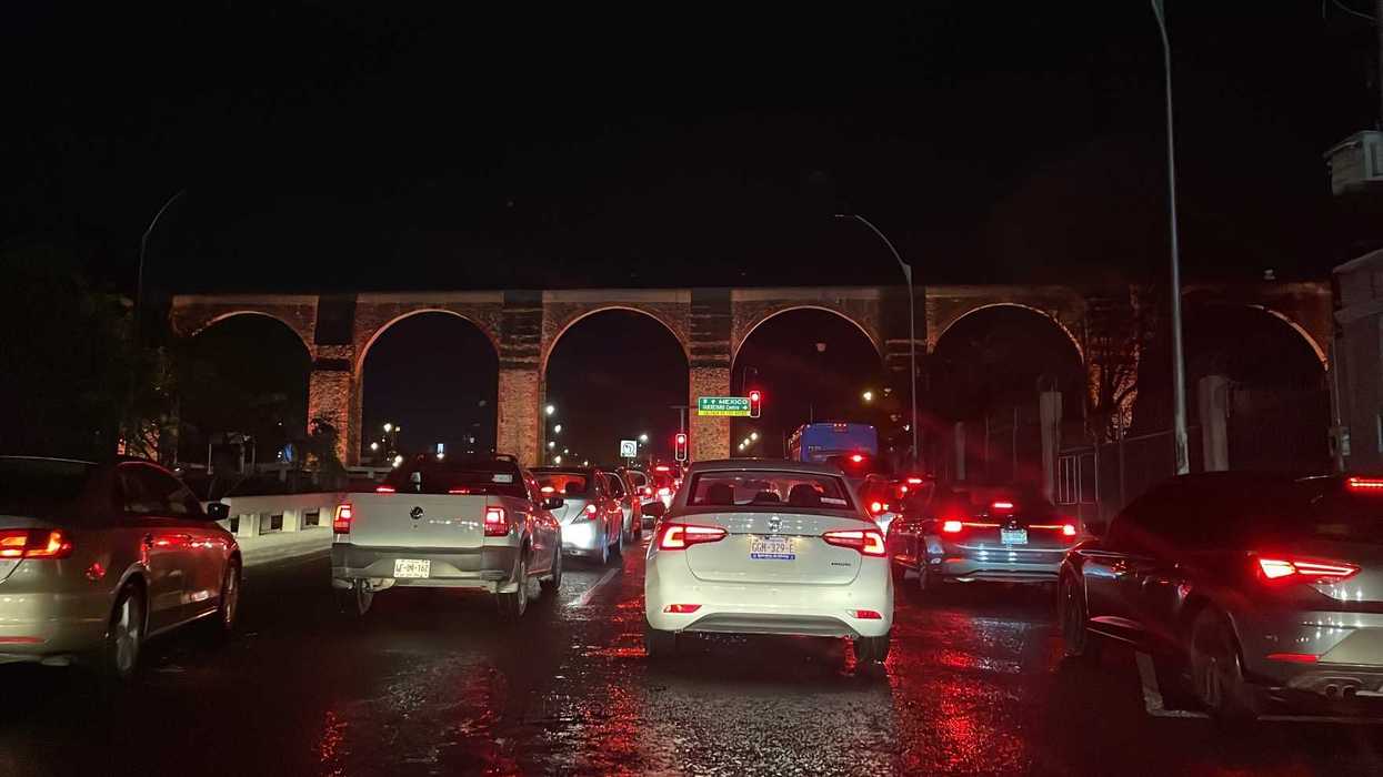 Fila de autos con luces traseras encendidas sobre el Acueducto de Querétaro durante la noche, con el pavimento mojado