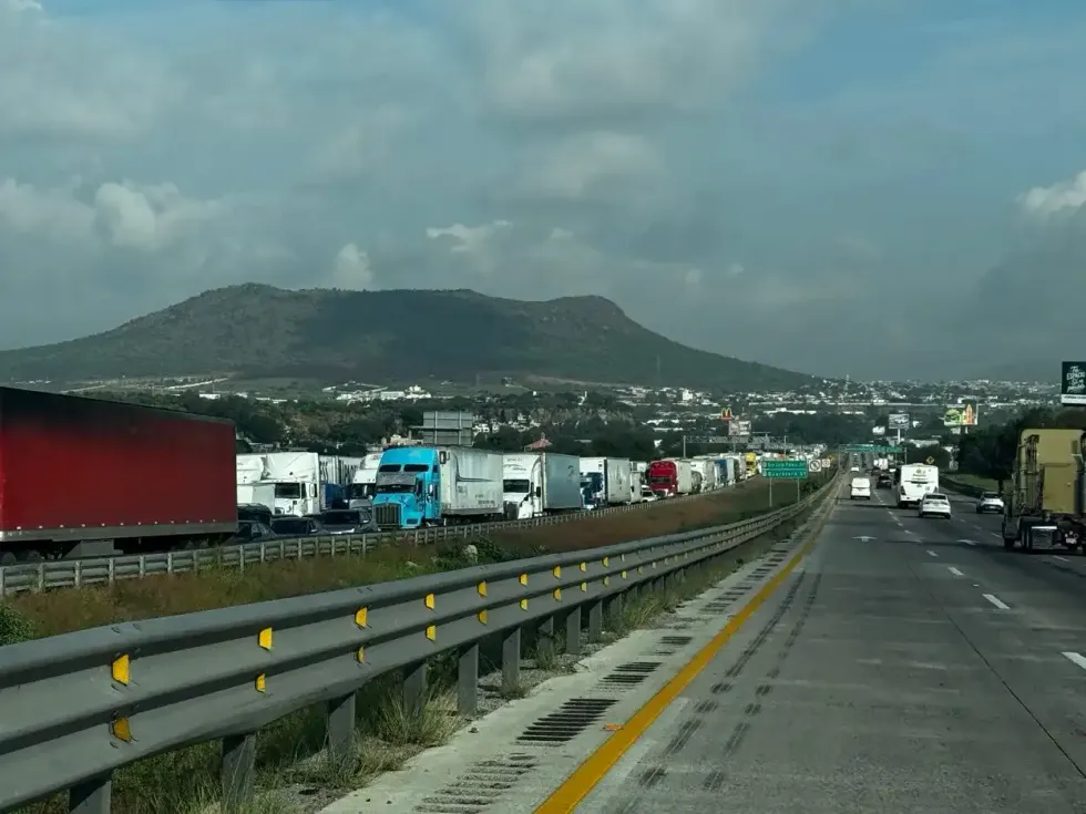 Fila de veh\u00edculos de carga detenidos junto a se\u00f1alamiento vial sobre la carretera federal 57