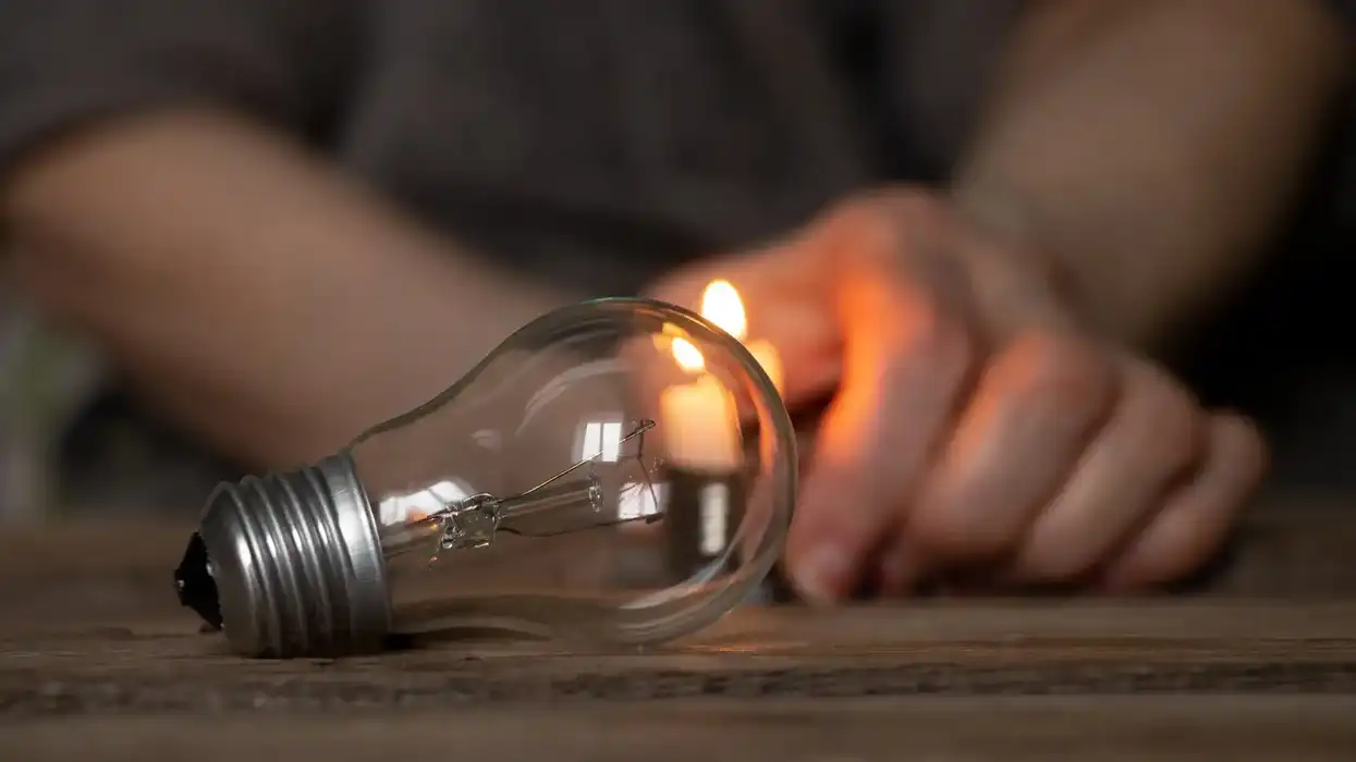 Foco apagado sobre una mesa de madera iluminada solo por una vela al fondo