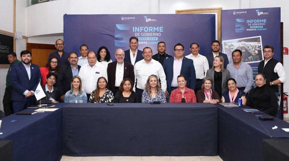 Fotograf\u00eda de grupo de asistentes a la reuni\u00f3n con la CANACO SERVyTUR en San Juan del R\u00edo, frente a una mampara del Quinto Informe de Gobierno 2025-2026.
