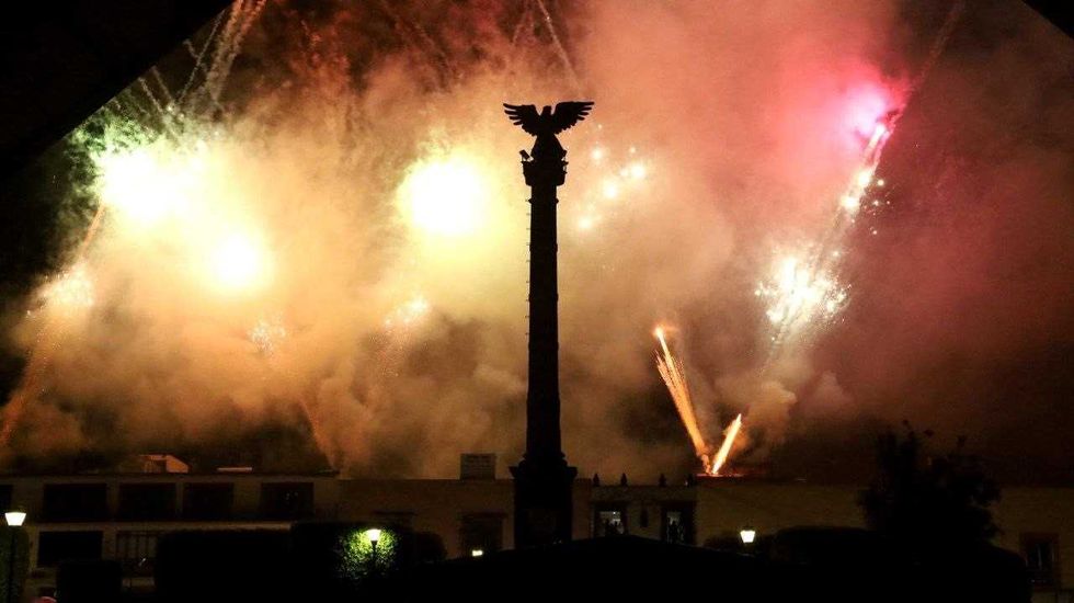 Fuegos artificiales iluminan el cielo detr\u00e1s de una columna coronada por un \u00e1guila.