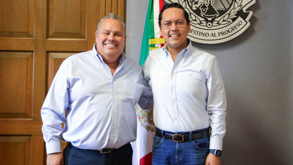 Gerardo Cuanalo Santos, director de la AMEQ, y Chepe Guerrero, presidente del Cabildo Metropolitano, posan sonrientes frente a la bandera nacional y el escudo del Estado de Querétaro.
