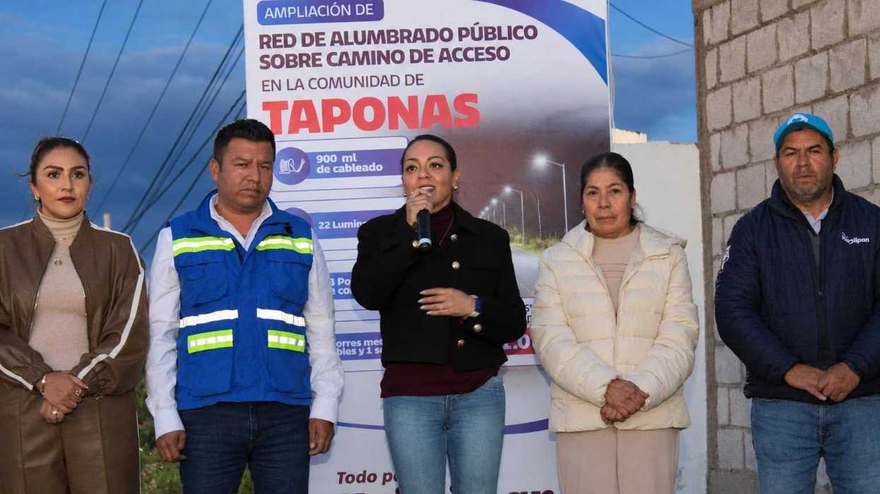 Ginna Guzmán habla con micrófono frente a la lona de la ampliación del alumbrado público en Taponas, Huimilpan