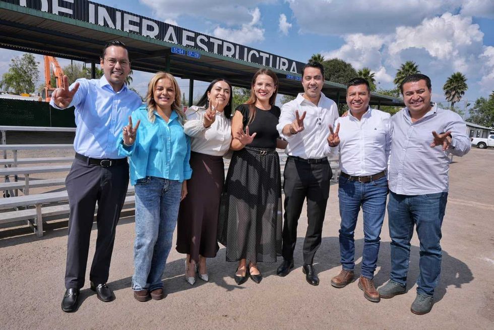 Grupo de personas hace la se\u00f1al de victoria bajo un letrero de infraestructura en el festejo del D\u00eda del Caminero