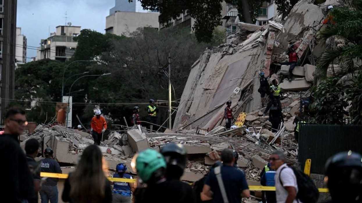 Grupo de personas remueve escombros de un edificio colapsado con montañas al fondo, en zona costera de Venezuela afectada por el terremoto