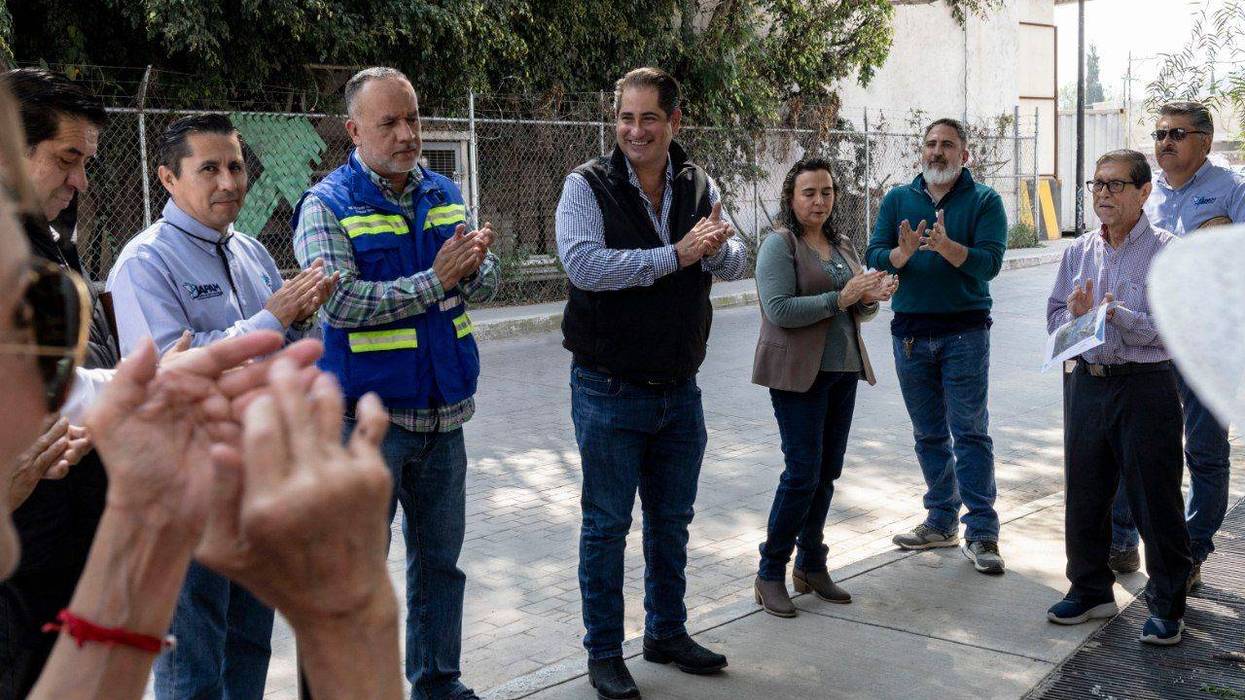Grupo de vecinos y funcionarios aplaude durante una reunión al aire libre en una calle.