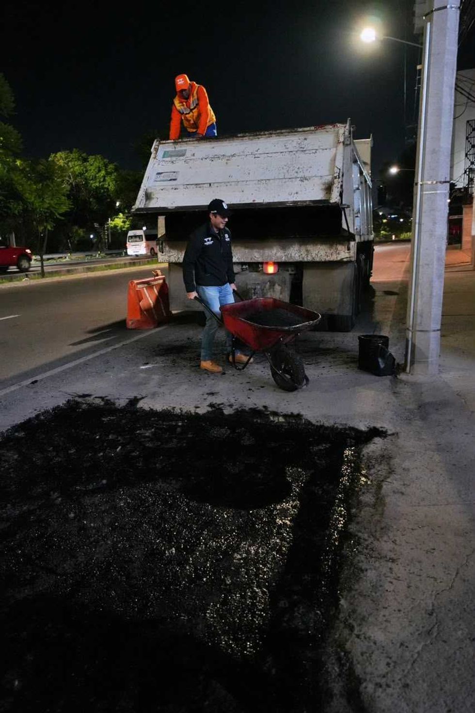 Hombre con carretilla de asfalto junto a un cami\u00f3n de volteo durante el bacheo nocturno en Quer\u00e9taro