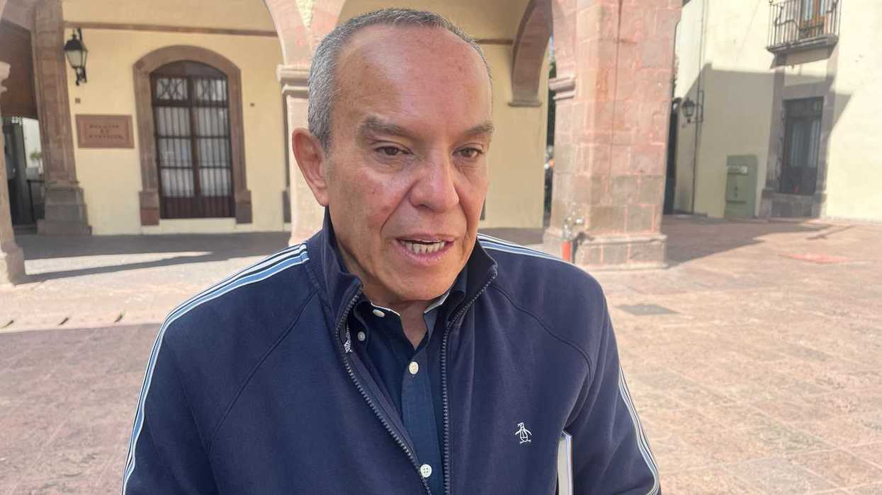 Hombre con chamarra azul habla frente a unos arcos de piedra; pronóstico de lluvias en Querétaro
