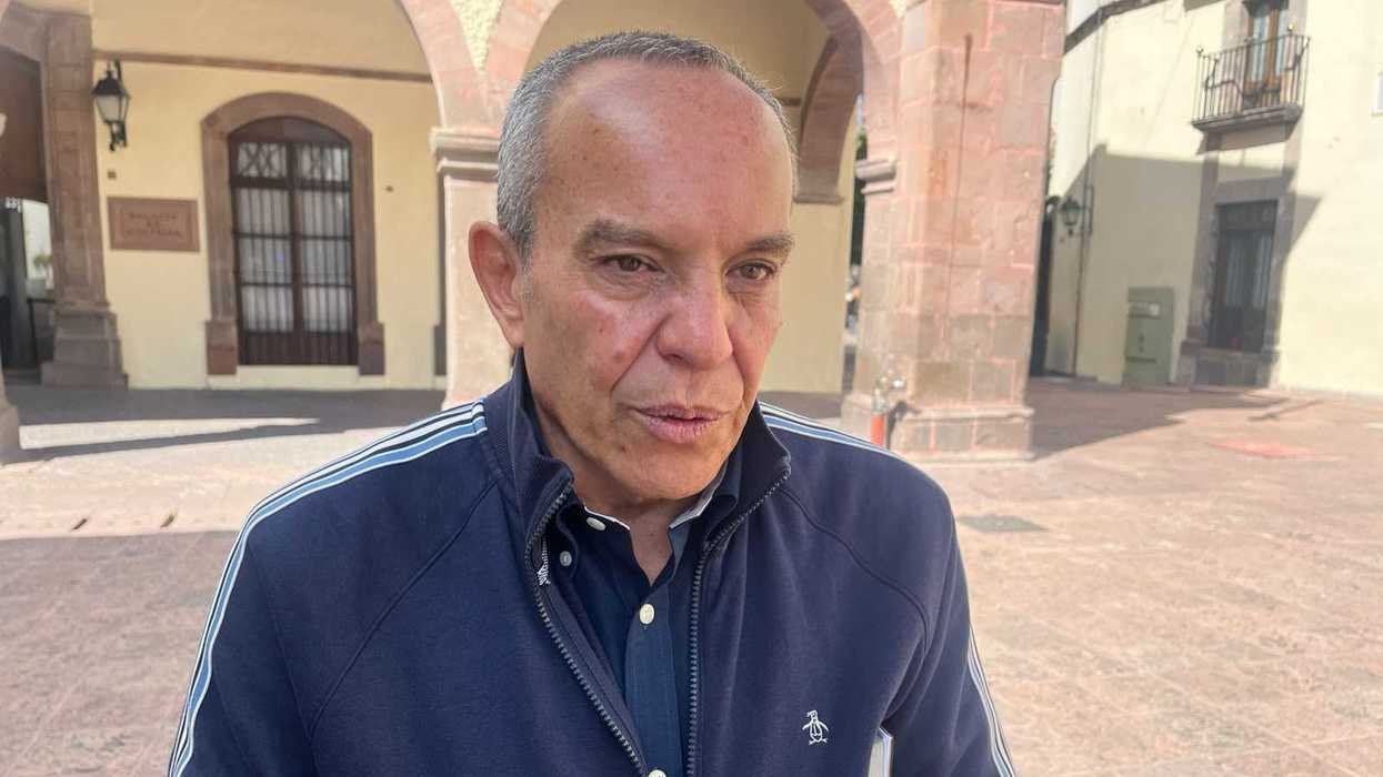 Hombre con chamarra azul marino habla ante un micrófono en una plaza; alerta por deslaves en la Sierra Gorda
