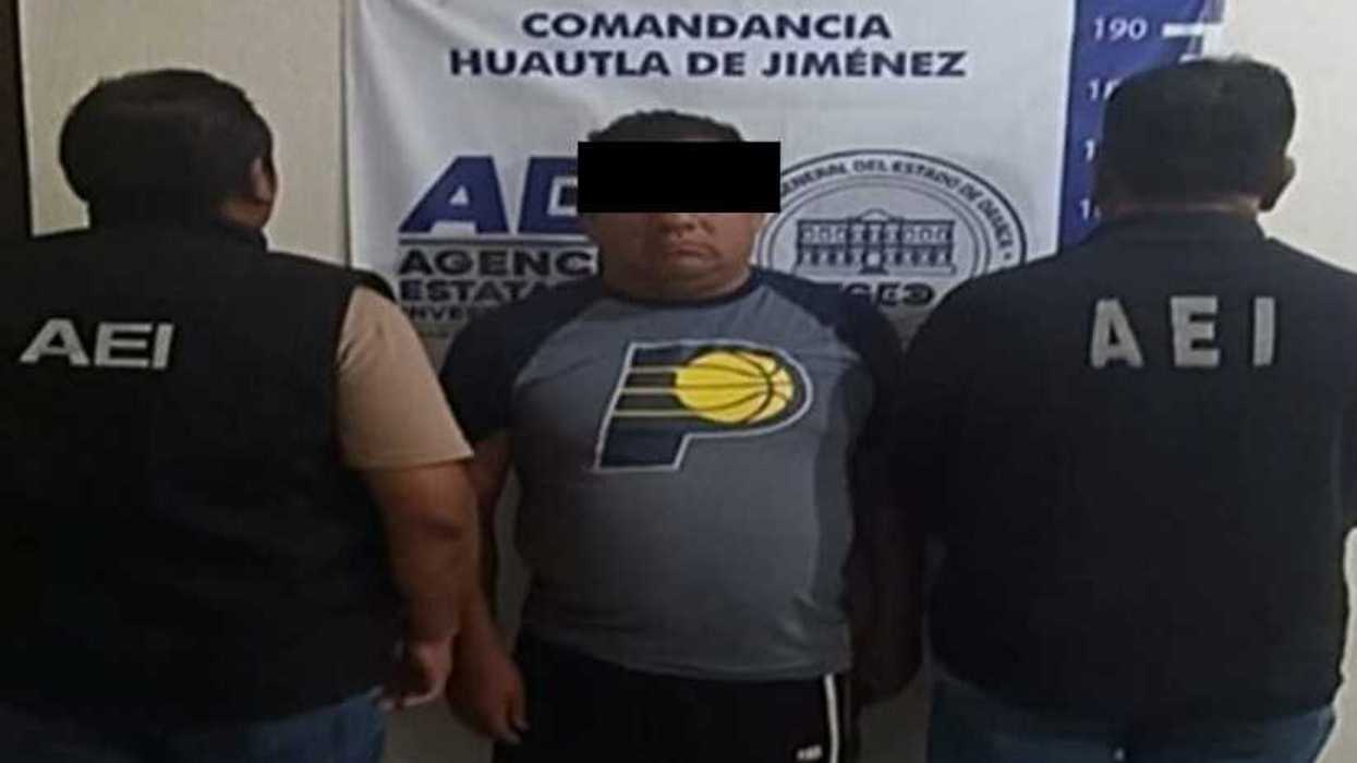 Hombre con el rostro cubierto junto a agentes de la AEI frente a una lona de la Comandancia Huautla de Jiménez, Oaxaca