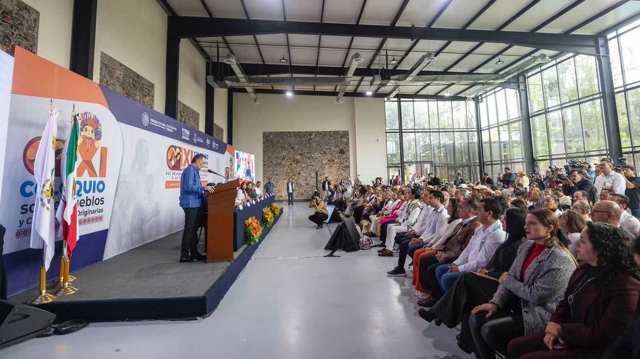 Hombre con guayabera blanca bordada habla en el podio del XI Coloquio