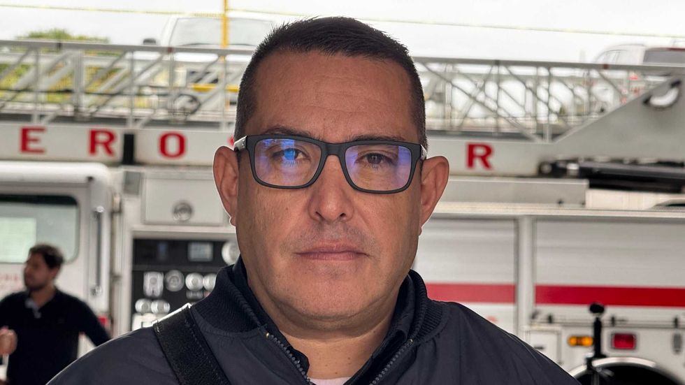 Hombre con lentes y chamarra oscura frente a una unidad con escalera del Cuerpo de Bomberos de San Juan del R\u00edo
