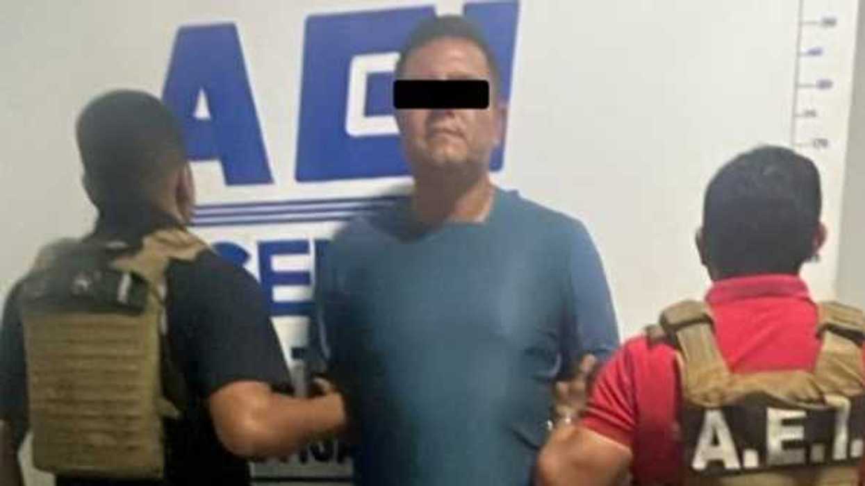 Hombre con los ojos cubiertos entre dos agentes con chalecos A.E.I., detenido por homicidio en centro de rehabilitación